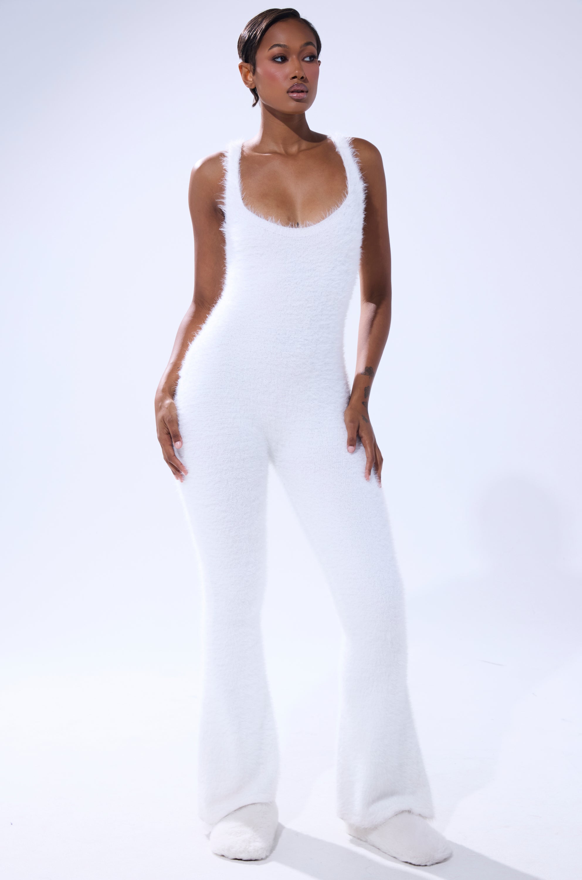 A person with short hair and natural makeup poses confidently against a white background in the STAYING IN FUZZY KNIT JUMPSUIT, a fitted sleeveless style with flared legs—modern loungewear at its best. 1
