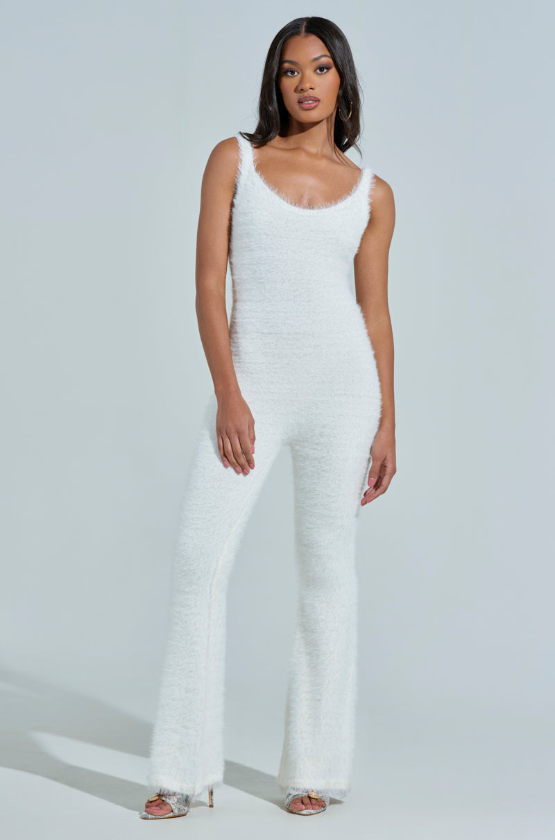 A woman with long dark hair poses in the STAYING IN FUZZY KNIT JUMPSUIT, a stylish sleeveless piece with flared legs made from faux mohair. She wears hoop earrings and open-toed heels, set against a plain light-colored background.