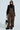 Against a light background, someone in PULL UP ON ME LEOPARD OVERALLS with adjustable buckled straps, a black turtleneck sweater, black platform shoes, and sunglasses holds a black handbag and has long hair draped over one shoulder.