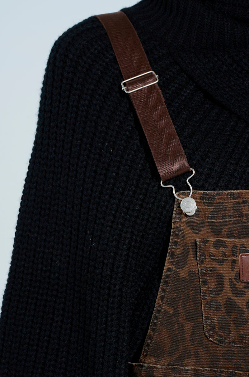 Close-up of a person in PULL UP ON ME LEOPARD OVERALLS, featuring adjustable buckled straps. The focus is on the dark ribbed sweater underneath and the clothing's texture and pattern with a metal clasp on the strap.