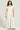 A person with long curly hair is wearing the YA YOU THOUGHT FRENCH TERRY JUMPSUIT, which features a wide-leg silhouette and an off-the-shoulder design crafted from a stretchy cotton blend in light beige. They are standing against a plain, light-colored background.