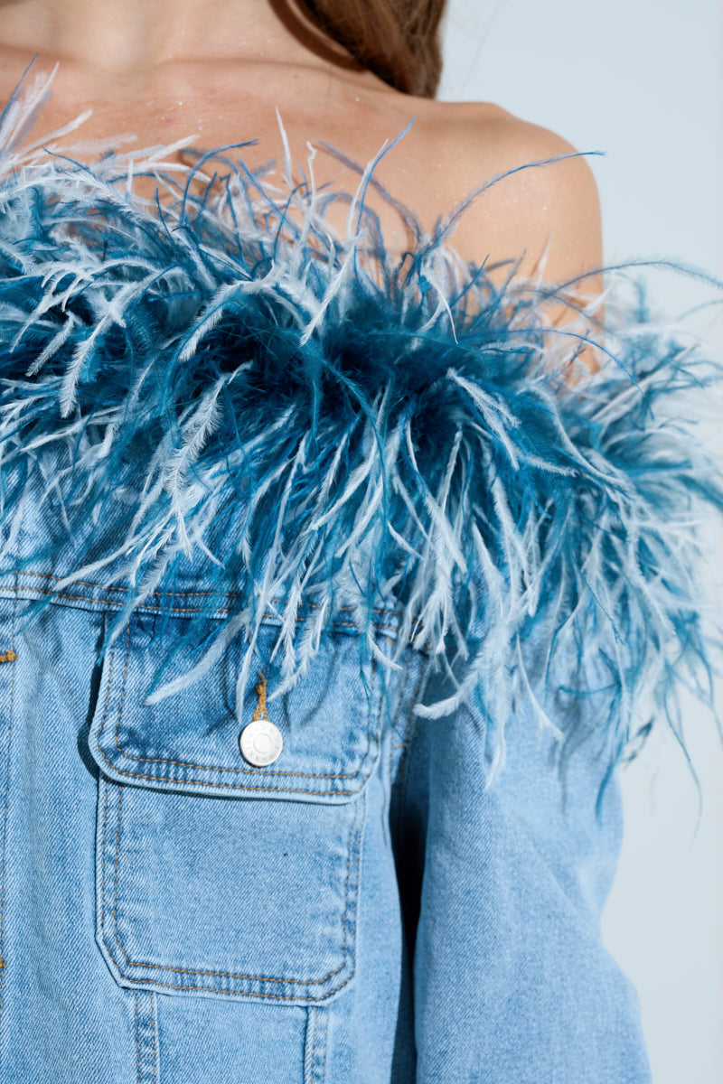 The CHIC AF DENIM MINI DRESS WITH FEATHERS features a close-up of an off-the-shoulder design, with blue and white feather trimming along the top. Visible stitching highlights the denim, while button details and lush feathers elegantly adorn the neckline.