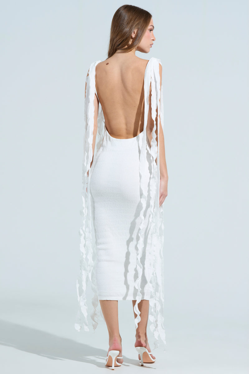 A woman faces away from the camera in a GET LIKE ME BACKLESS MIDI DRESS IN IVORY featuring flowing textured fabric strips. Her long brown hair cascades down as she wears white high-heeled sandals, all set against a light blue background, showcasing her elegant, curve-hugging silhouette.