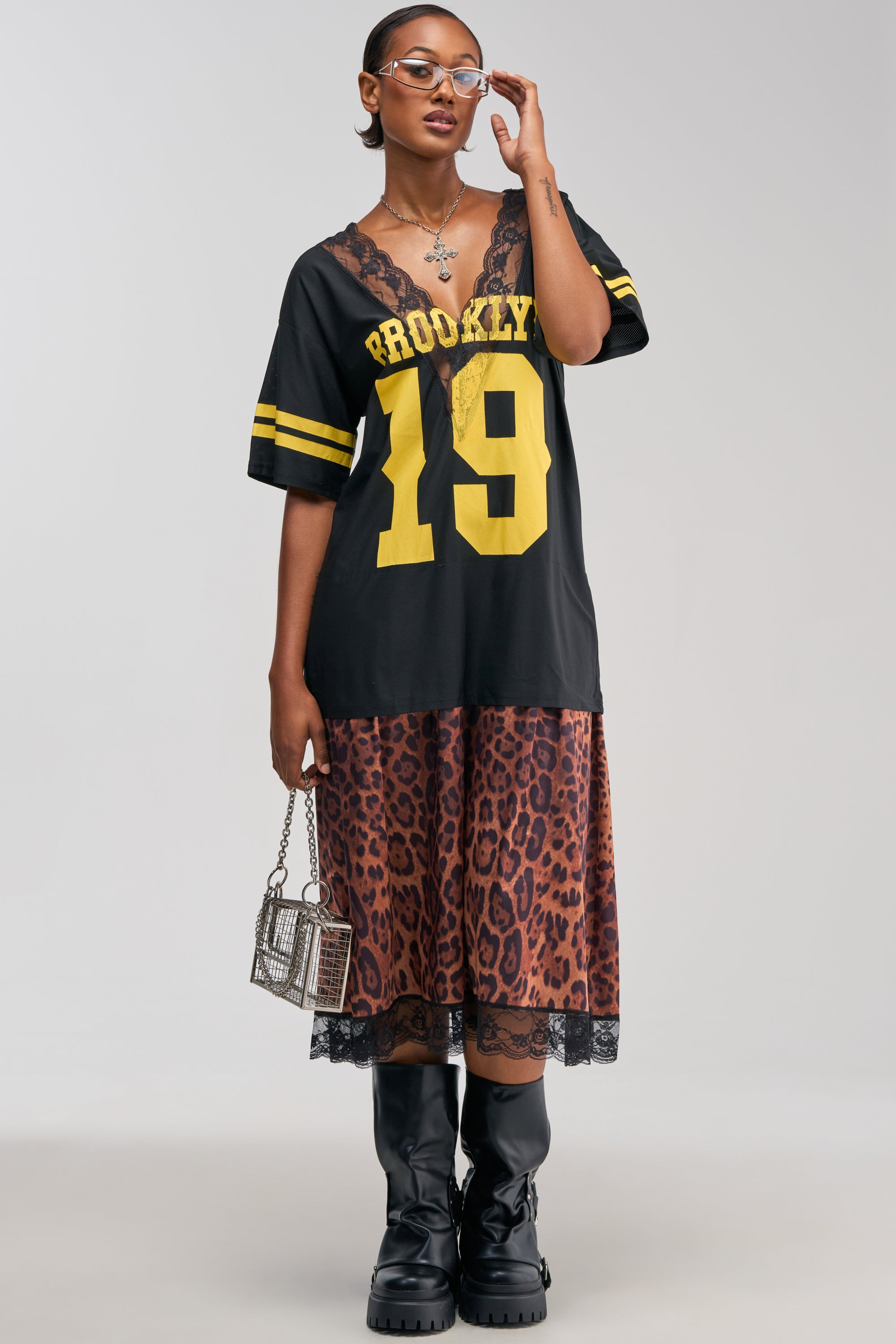 A person wearing the “CITY GIRL LAYERED JERSEY MAXI DRESS,” styled with streetwear flair, paired with black boots, glasses, a necklace, and holding a small box-shaped purse against a plain background.