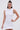 A woman in the IDK FELT CUTE RIBBED KNIT MINI DRESS, a sleeveless fitted mini with a rolled collar, stands confidently against a plain background. She wears her long dark hair in a top knot and accessorizes with large hoop earrings.