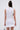 A person with long, dark hair in a topknot wears the IDK FELT CUTE RIBBED KNIT MINI DRESS, a sleeveless, fitted white mini dress, and holds a small handbag. They have a round patch on their upper left arm; the background is plain light gray.