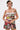 A woman with tattoos and short, dark hair with a blonde streak models the STREETS ARE CALLING PRINTED RUFFLE ROMPER—a colorful, strapless one-piece with graphic prints—standing confidently against a plain white background.