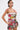 Model with short dark hair and geometric earrings poses against a white background, wearing the STREETS ARE CALLING PRINTED RUFFLE ROMPER, a strapless one-piece with colorful abstract patterns and ruffle details; unique tattoos on upper arms.