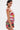 A woman with short dark hair models the STREETS ARE CALLING PRINTED RUFFLE ROMPER in a streetwear style, accessorized with large geometric earrings and pink paint on her shoulder, set against a white backdrop.