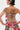 A person with short dark hair and visible tattoos wears the STREETS ARE CALLING PRINTED RUFFLE ROMPER, showcasing bold streetwear style and intricate tattoo art. The image highlights the romper’s colorful print, ruffle details, and unique open-back design.