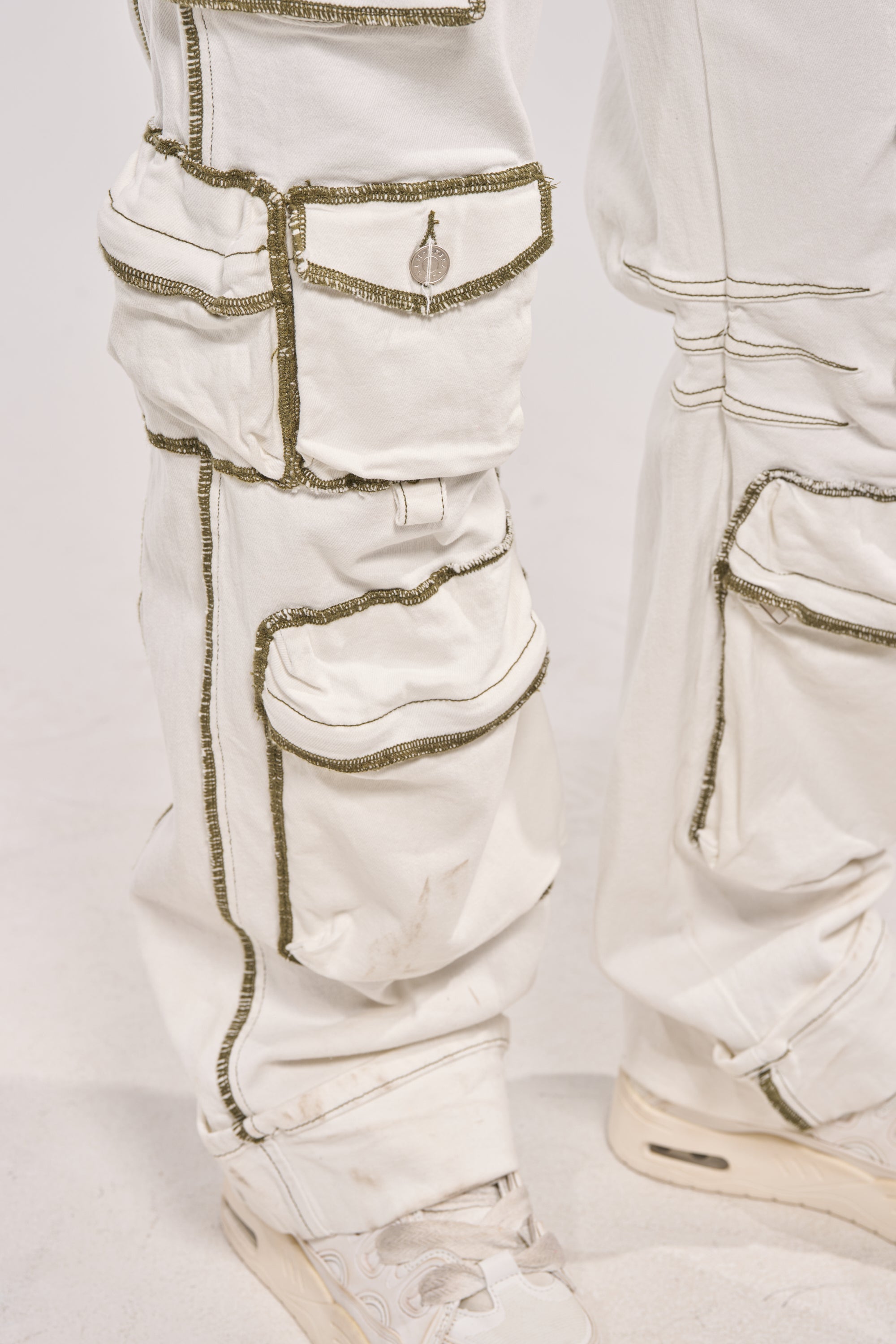 Close-up of the BROOKLYN UTILITY DENIM JUMPSUIT featuring white denim, multiple pockets, dark stitching, and a slightly baggy fit. Styled with white sneakers for a casual, utilitarian look inspired by classic cargo jumpsuits. 6