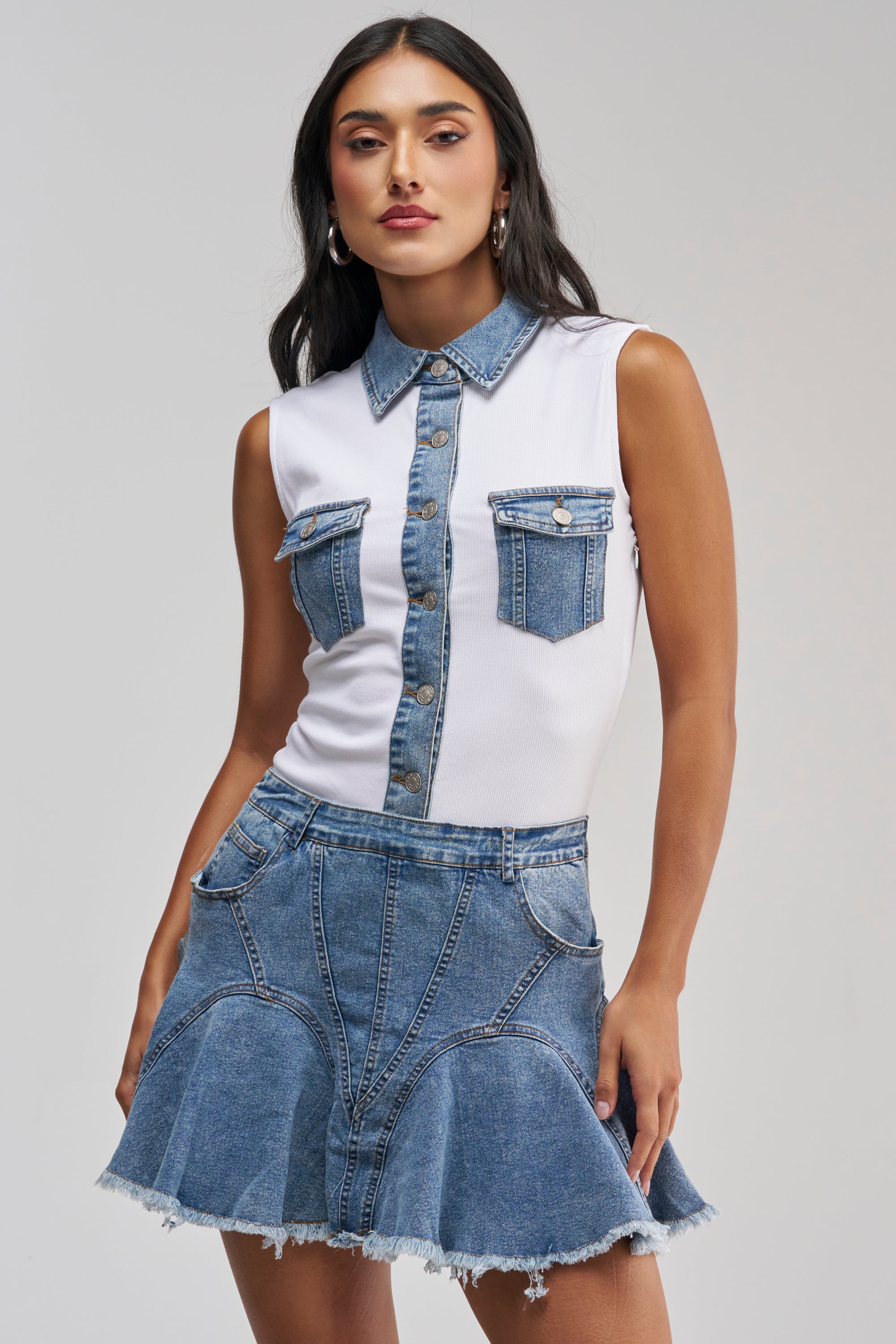 Model showcases effortless casual styling in the JULIETTE KNIT DENIM SLEEVELESS MINI DRESS, featuring a white sleeveless silhouette with denim trim and a frayed hem, set against a plain light background.