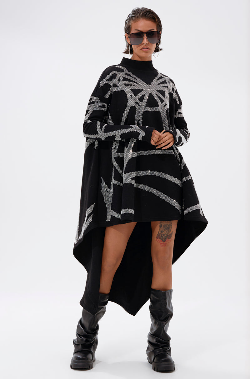 A woman confidently poses against a white background wearing the LANIE PRINTED RHINESTONE SWEATER DRESS with silver abstract lines, paired with black knee-high boots, large sunglasses, and hoop earrings.