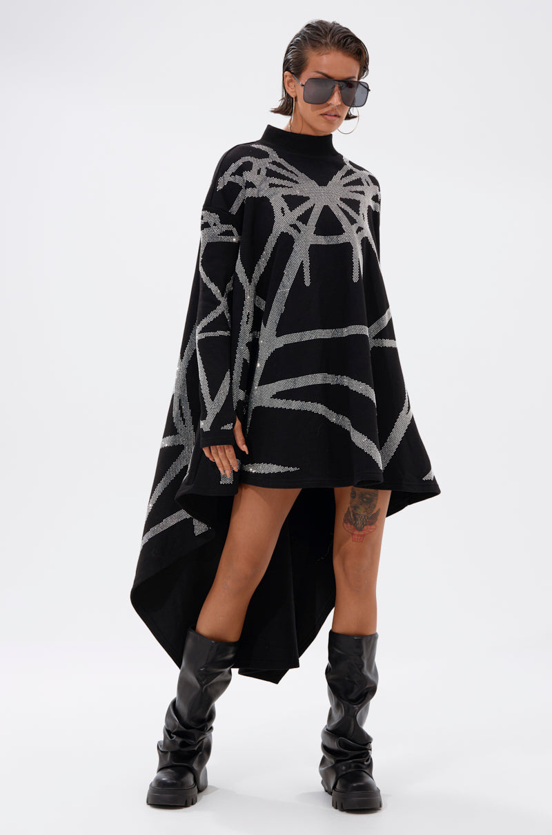 A woman models the LANIE PRINTED RHINESTONE SWEATER DRESS—an oversized black dress with silver abstract lines—styled with black knee-high boots and large sunglasses, confidently posing against a plain white background.