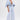 A person with short dark hair stands confidently against a white background, wearing the BORN TO STAND OUT DENIM JUMPSUIT featuring a plunging V-neckline and wide-leg silhouette.