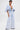 A person with short dark hair stands confidently against a white background, wearing the BORN TO STAND OUT DENIM JUMPSUIT featuring a plunging V-neckline and wide-leg silhouette.
