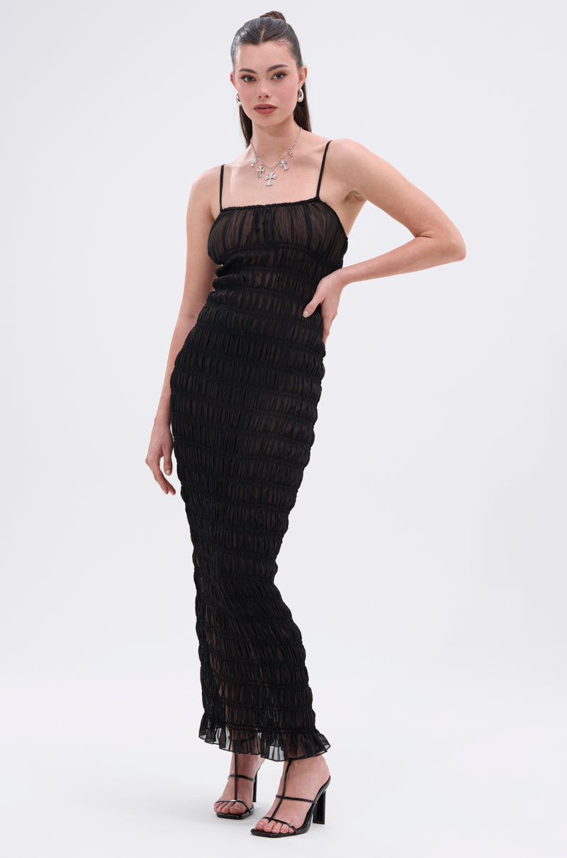 A woman poses against a plain background in the ON A BEACH OR A NIGHT OUT MESH MAXI DRESS. The figure-hugging mesh maxi features thin straps and chic style, perfect for day-to-night wear. She accessorizes with black heels and a silver necklace.