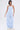 A woman faces forward wearing the SUCKER FOR YOU SEERSUCKER JUMPSUIT with a strapless neckline, wide leg silhouette, and cargo pockets, paired with white sneakers and layered silver necklaces. She has a sleek bob; background is plain white.