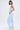 A woman in profile models the SUCKER FOR YOU SEERSUCKER JUMPSUIT—a light blue, strapless, wide-leg jumpsuit with cargo pockets. She pairs it with white sneakers, a chunky silver necklace, hoop earrings, and has straight dark hair.
