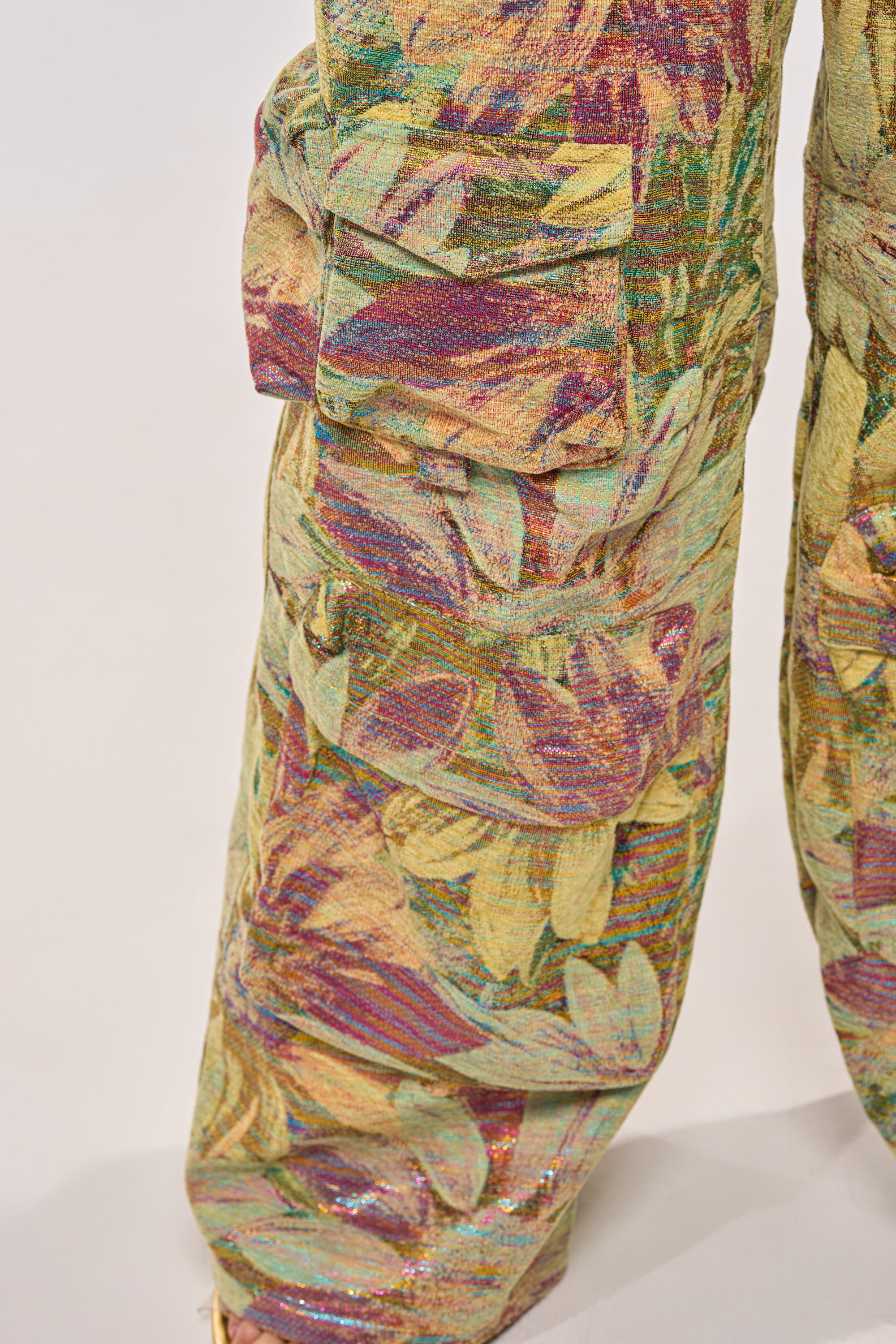 Close-up of the SMELL THE FLOWERS BROCADE STRAPLESS JUMPSUIT, featuring colorful, textured floral brocade in yellow, green, purple, and red with visible cargo pockets. 6