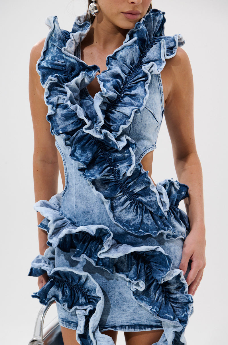 A woman wears the SAY IT AGAIN RUFFLED DENIM MINI DRESS, featuring bold vertical and diagonal ruffles across the front for a textured, statement-making look.