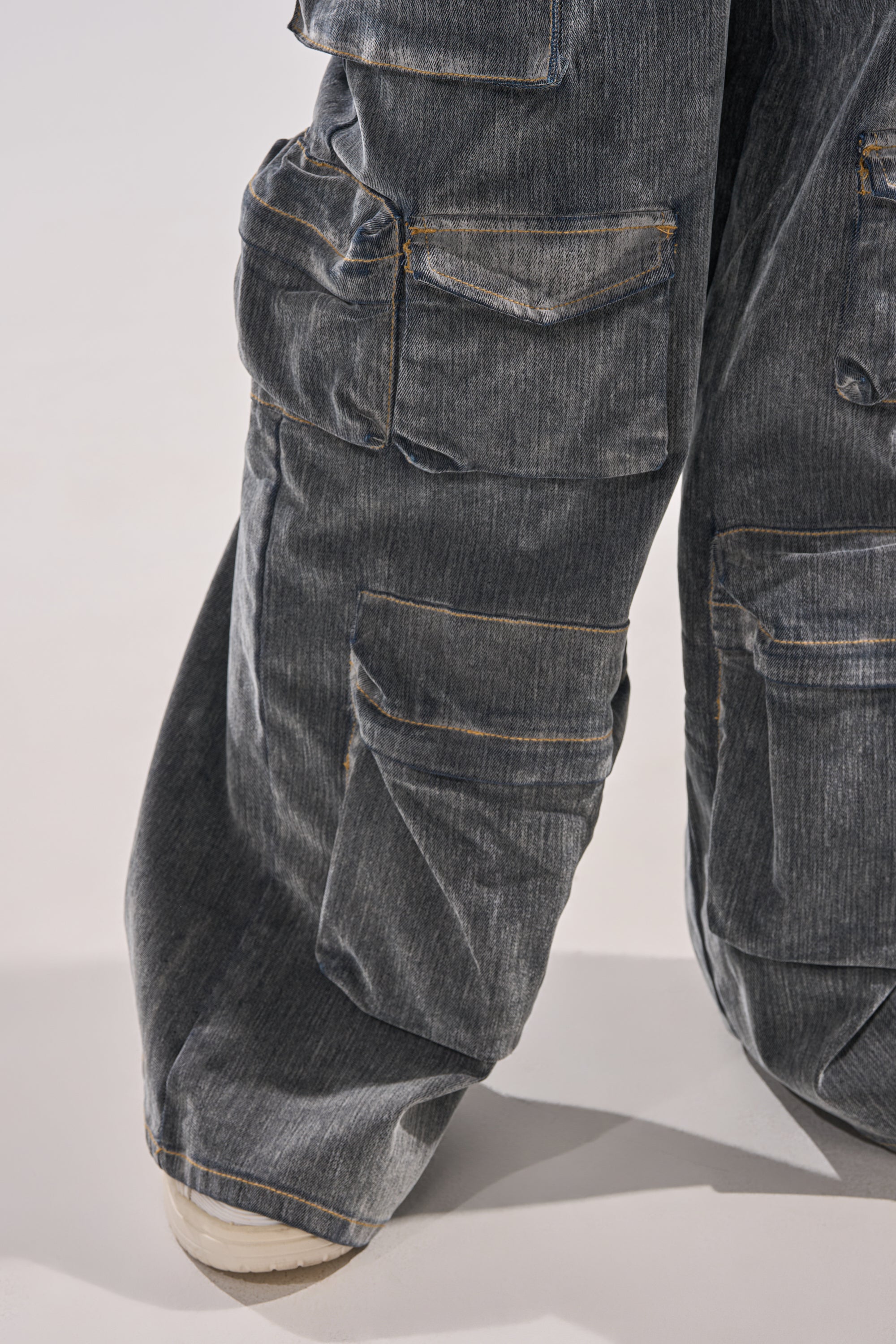 Close-up of a person wearing the MELINDA VELVET JUMPSUIT, styled with a relaxed fit, featuring multiple large pockets and visible stitching; the hem drapes over part of a white shoe. 10