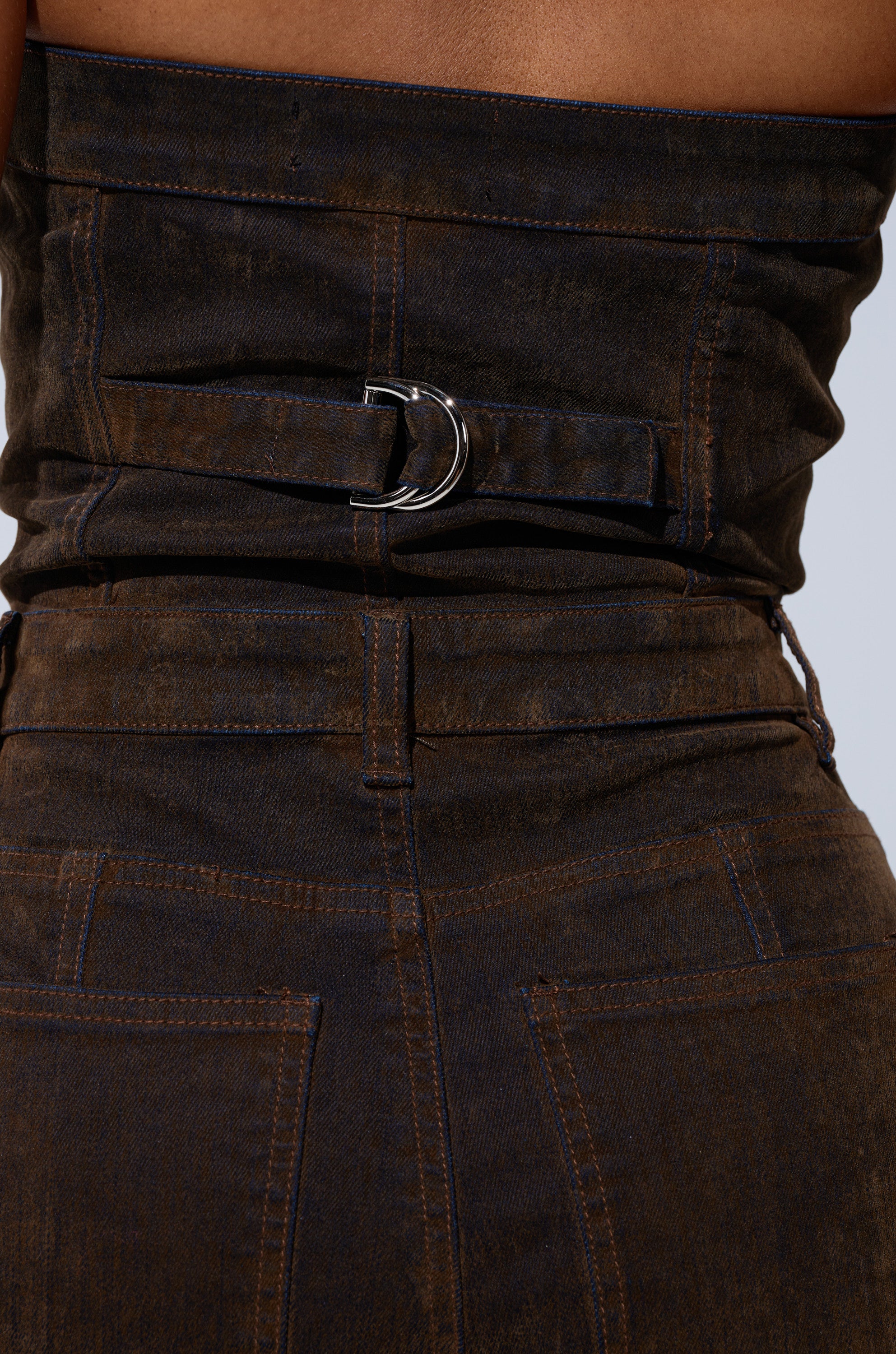 Close-up of the back of the ALICIA CROPPED CARGO JUMPSUIT, a high-waisted, dark denim wide-leg style with a silver buckle belt and visible stitching above two back pockets.