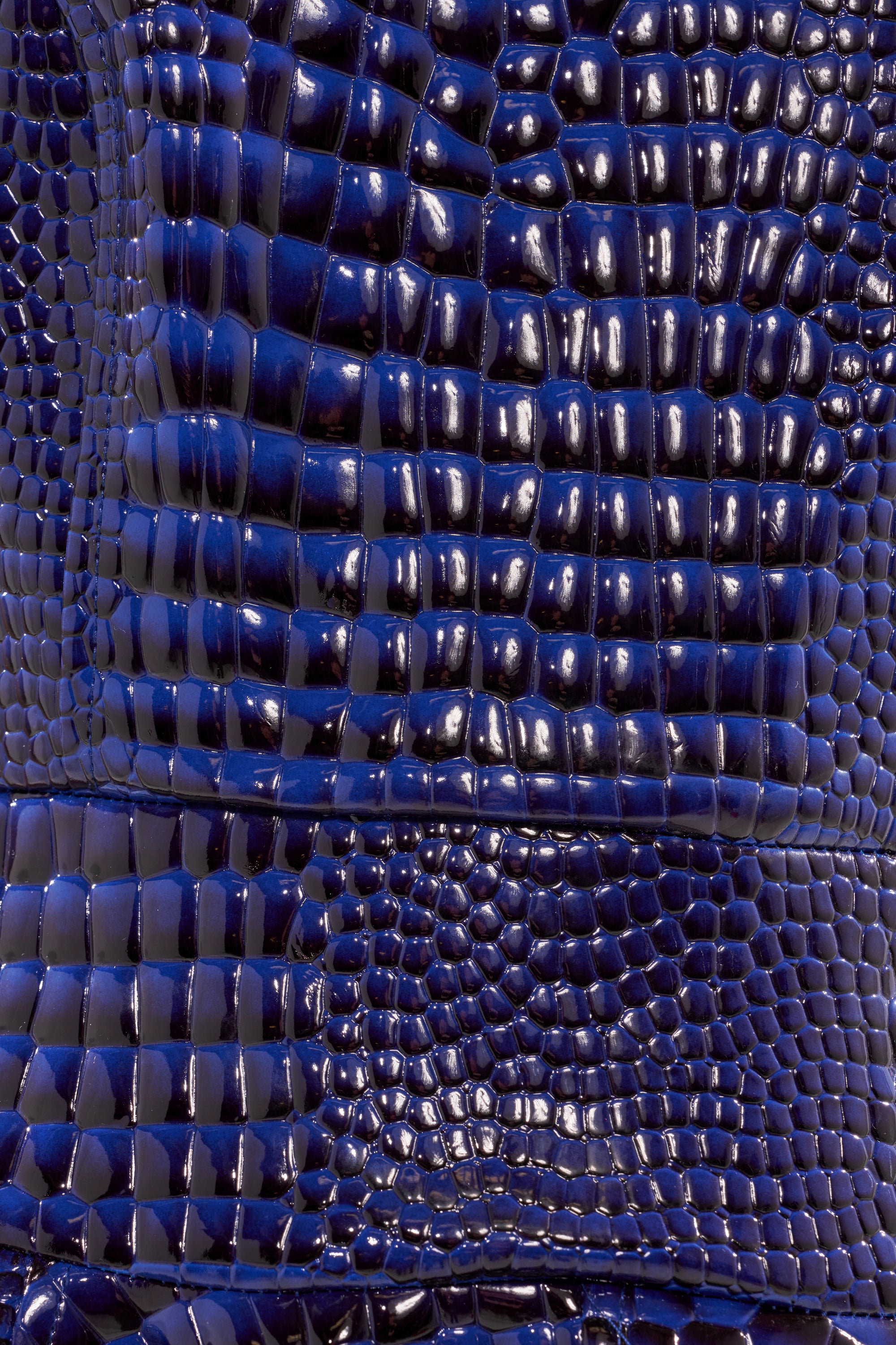 Close-up of the VEE FAUX LEATHER CROC MIDI DRESS, showcasing a shiny, dark blue crocodile-embossed surface with rectangular and square patterns that reflect light.