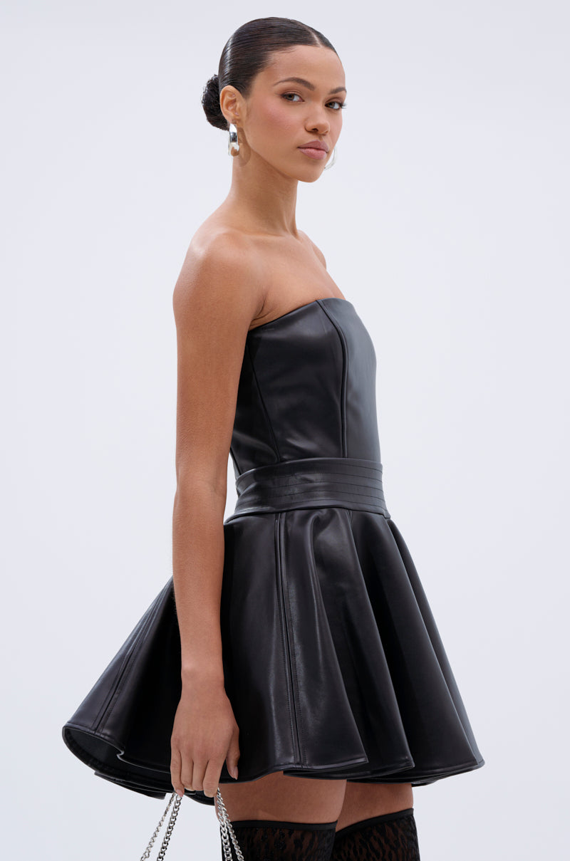 Woman wears the VAL PU MINI DRESS, a strapless faux leather skater-style dress with a fitted waist, paired with silver hoop earrings and a silver chain bag, posing against a plain white background.