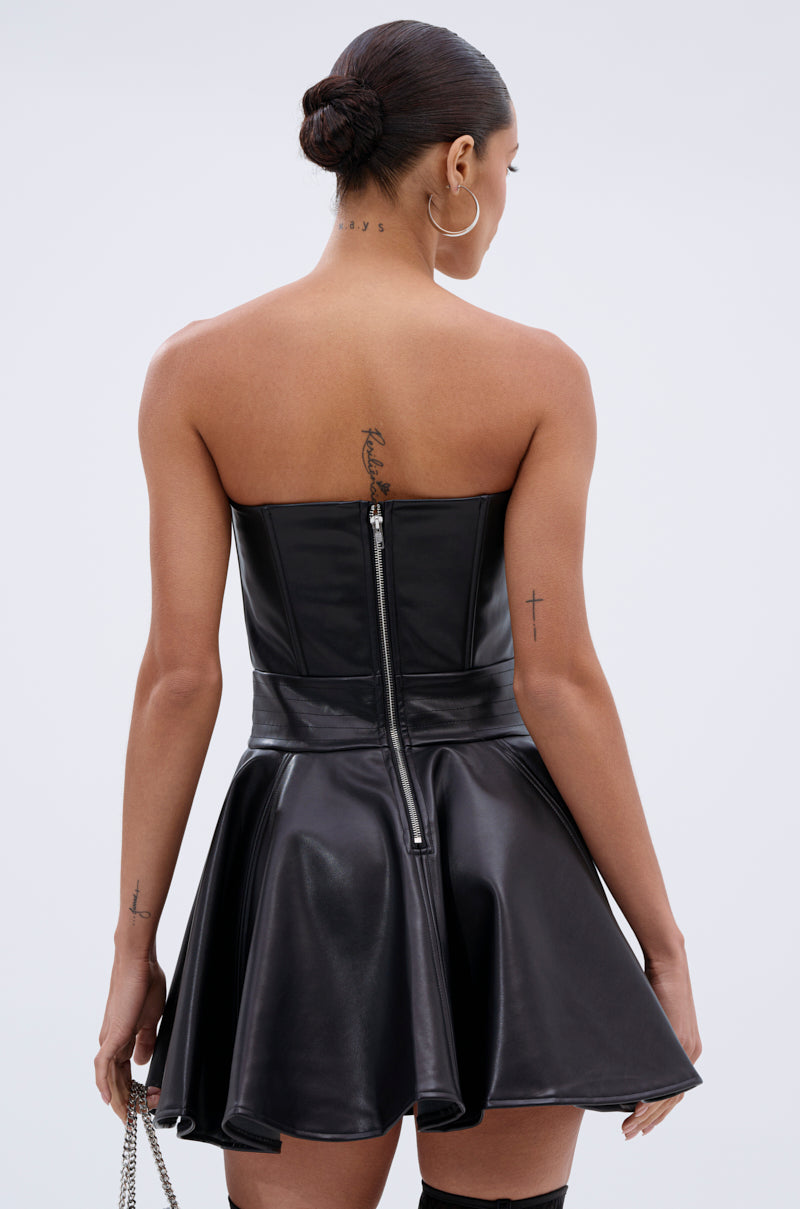 A woman with an updo, hoop earrings, and visible tattoos is seen from behind wearing the VAL PU MINI DRESS—a strapless faux leather skater-style dress with a flared skirt and back zipper—against a plain background.