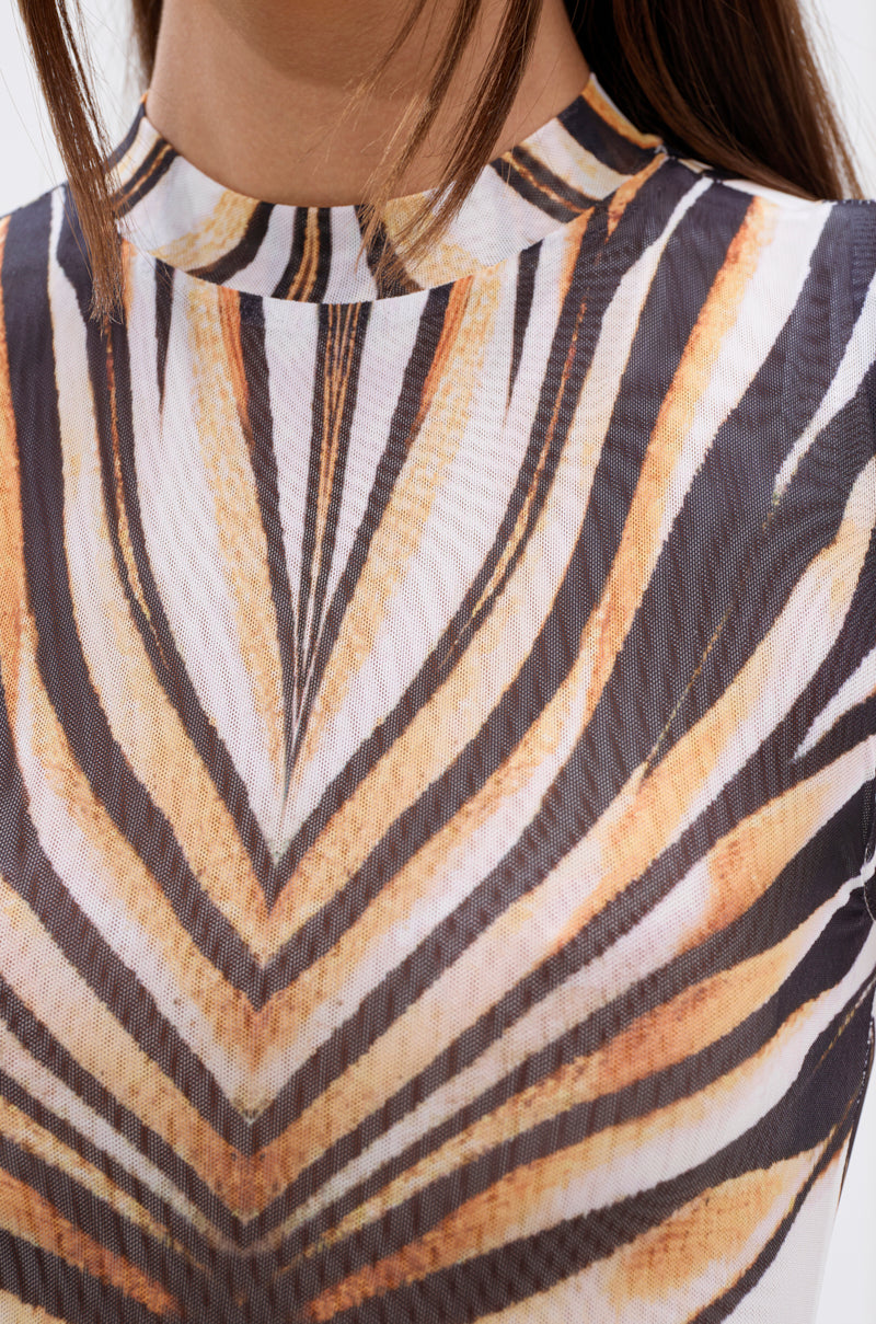 Close-up of a person wearing THE BOY'S ALL MINE PRINTED MIDI DRESS, featuring a sheer high-neck design with bold geometric orange, black, and white patterns resembling stylized zebra stripes. Only the neck and upper chest are visible. 4