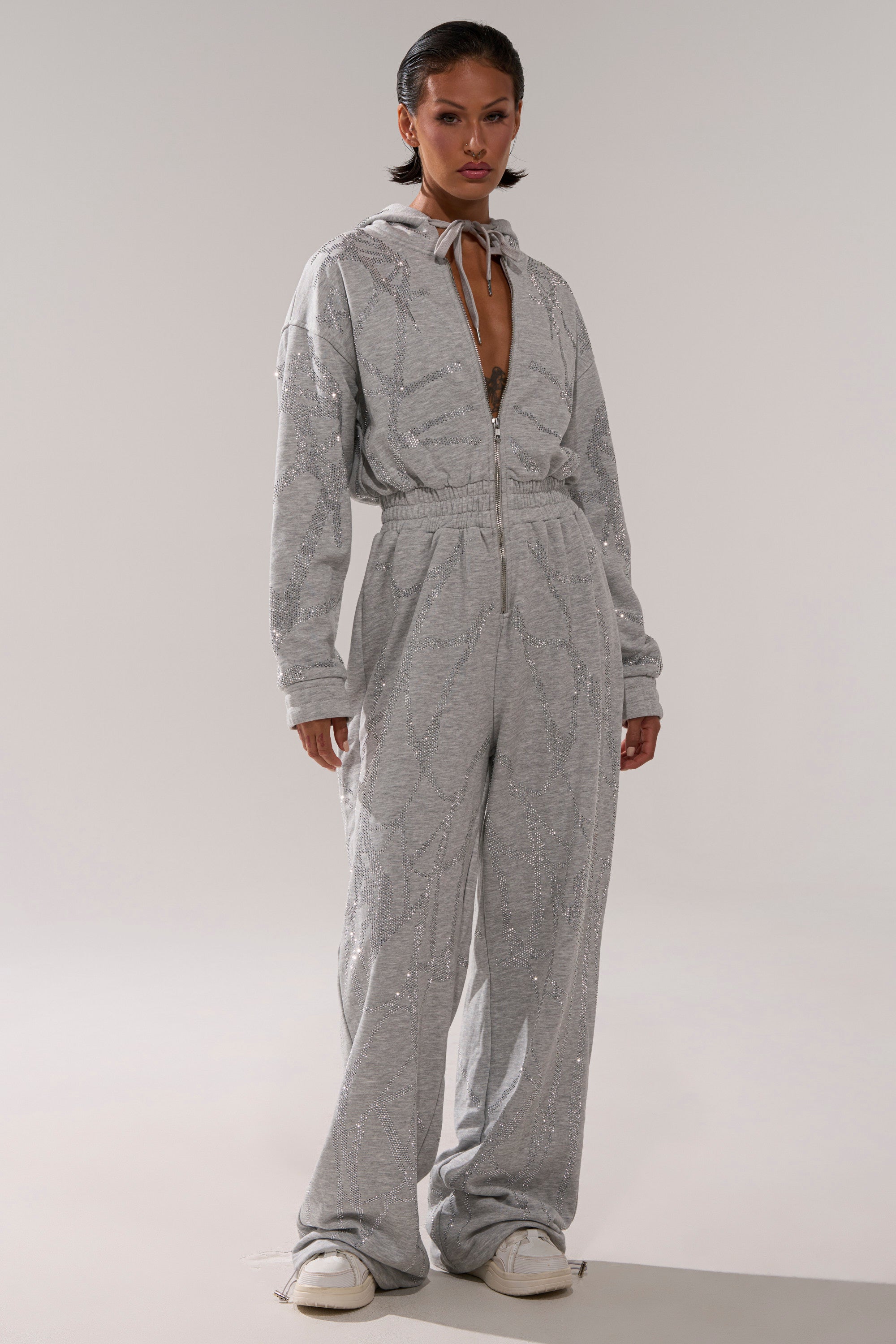 A woman wears the NEVER BUGGIN PRINTED FRENCH TERRY JUMPSUIT, a grey loungewear piece.