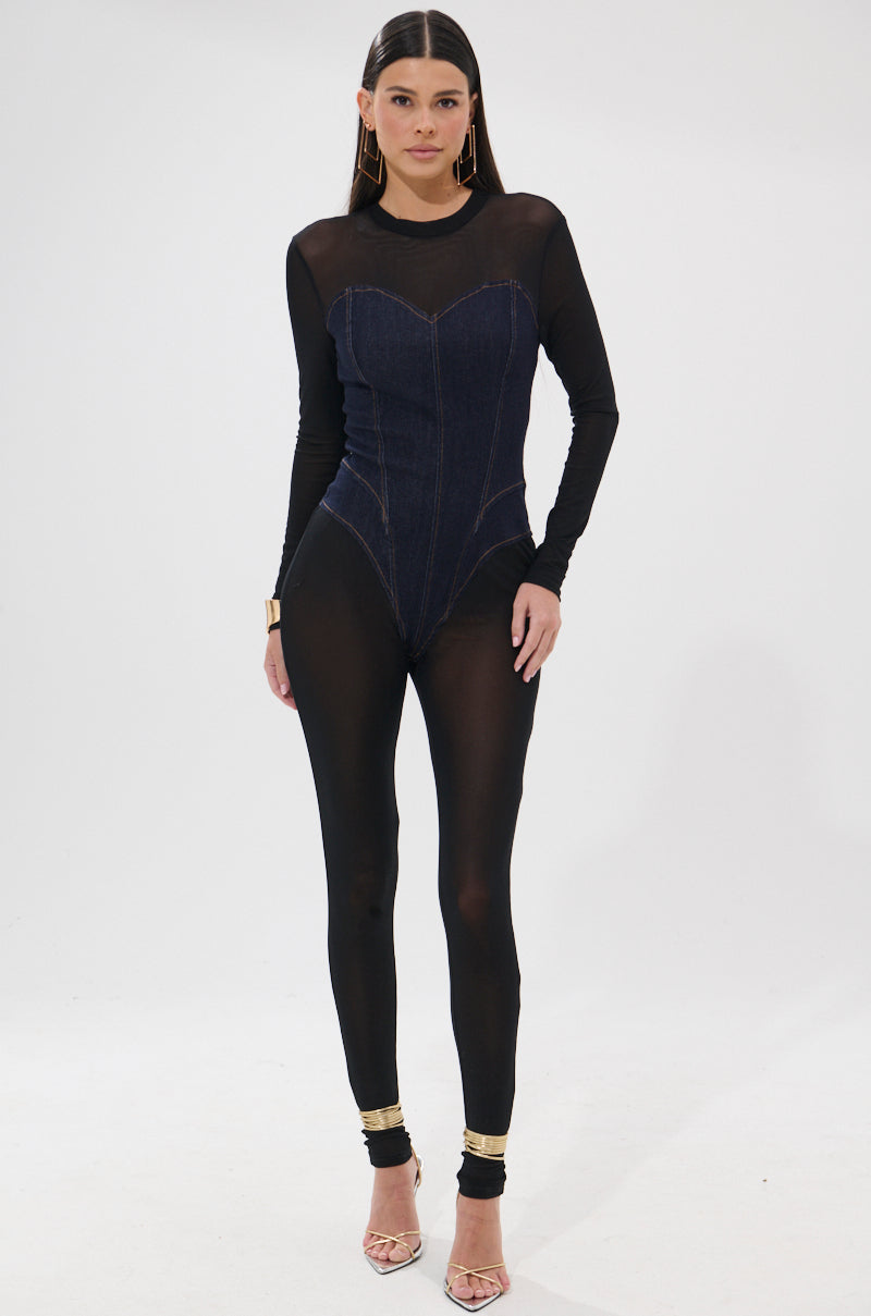 A woman poses against a white background in the NEW YEAR SAME ME MESH DENIM JUMPSUIT, featuring a corset bodice and sweetheart neckline, styled with gold anklets and open-toe high-heeled sandals.