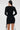 A woman with long straight hair is seen from behind wearing the RUN THIS TOWN LACE UP MINI DRESS, featuring lace-up details on the sides and sleeves. She stands against a plain light background, emphasizing its sleek bodycon silhouette.
