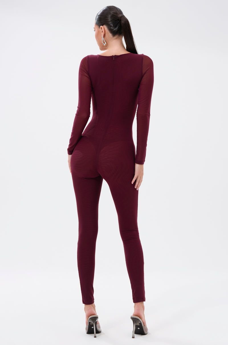 A woman with long dark hair in a ponytail models the KEEPIN IT SIMPLE MESH JUMPSUIT IN BURGUNDY, featuring a fitted skinny-leg design. She stands with her back to the camera against a plain white background, wearing high-heeled sandals. 4