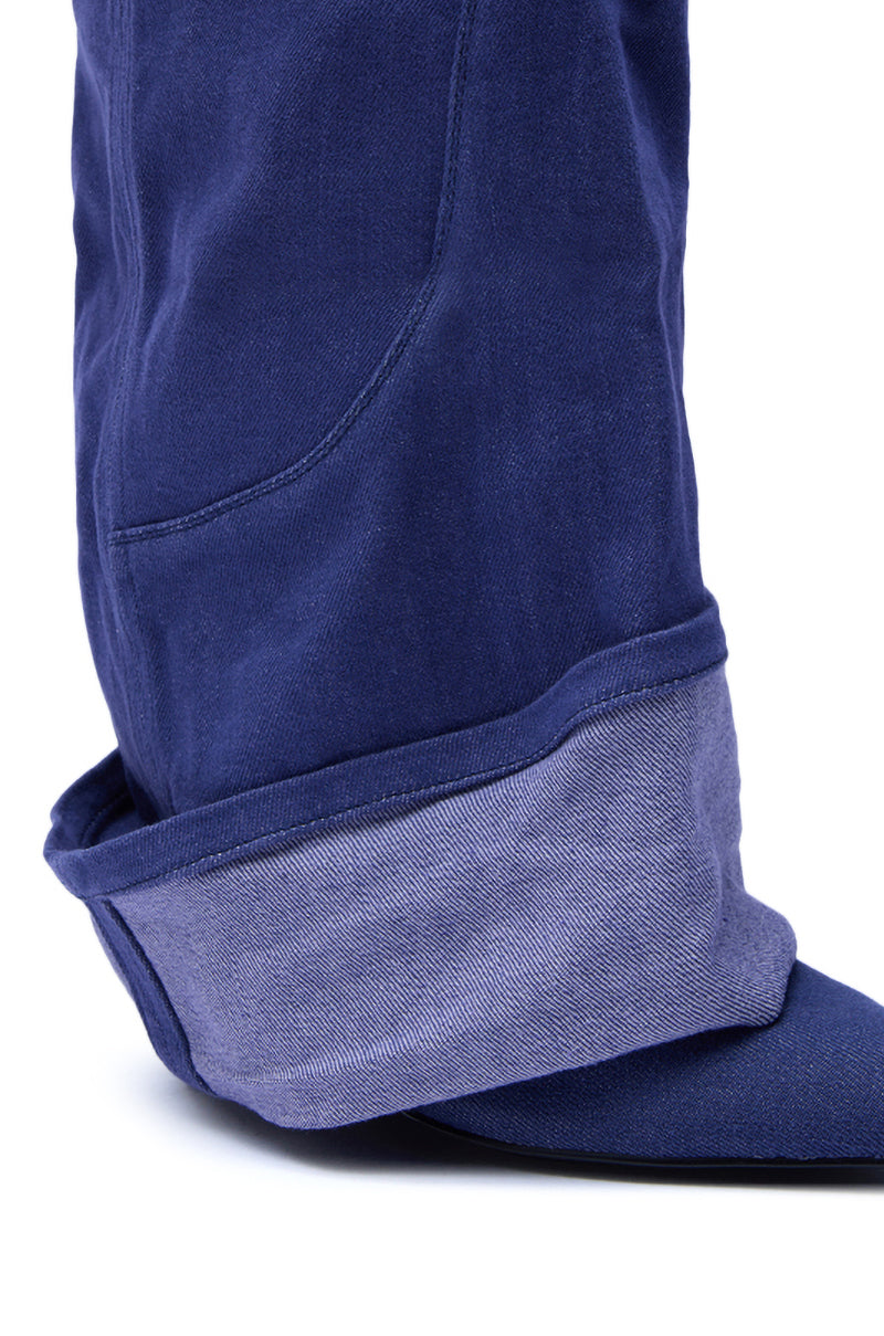 A close-up of the lower part of a blue denim pant leg with a thick cuff exposes the lighter inner fabric, draping over the pointed toe AZALEA WANG JATIN DENIM CUFF FOLD OVER WEDGE BOOTIE.