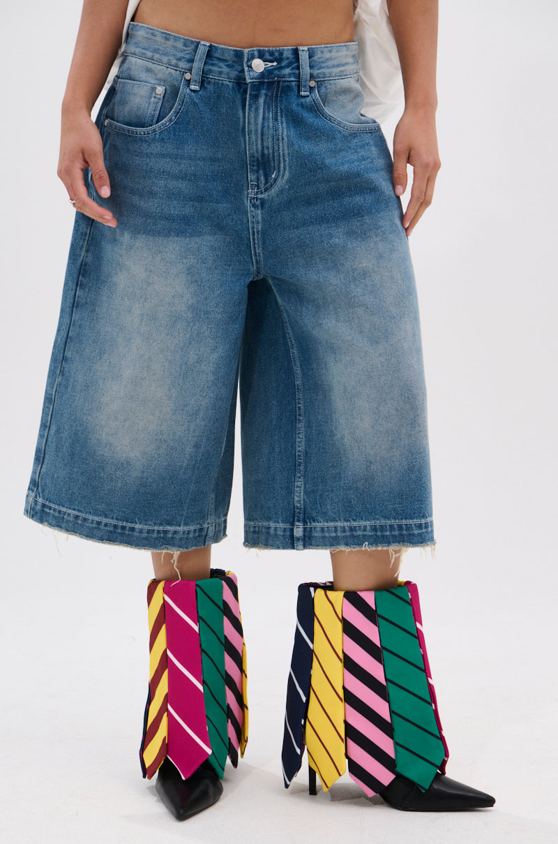 A person wears knee-length denim shorts and the AZALEA WANG JAUNE BLACK TIE BOOTIE, featuring a pointed toe and colorful striped fabric panels in green, pink, yellow, and red, standing against a plain white backdrop.