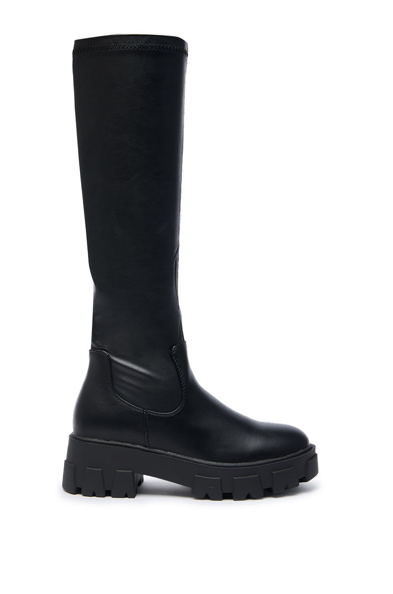The AZALEA WANG JAYE KNEE HIGH BOOT IN BLACK features a smooth leather finish and a chunky, textured sole, displayed in a side profile against a white background.