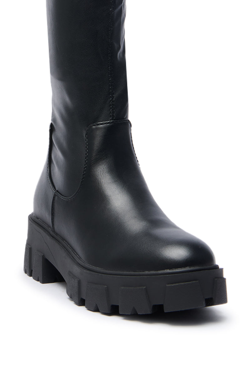 A close-up of the AZALEA WANG JAYE KNEE HIGH BOOT IN BLACK, showcasing its black leather, chunky textured sole, and smooth minimalist design, photographed against a white background.