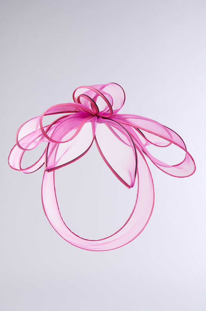 The TO THE RACES FASCINATOR IN PINK features delicate flowing loops and an oversized bow, forming a floral-inspired design against a plain light gray background. 2
