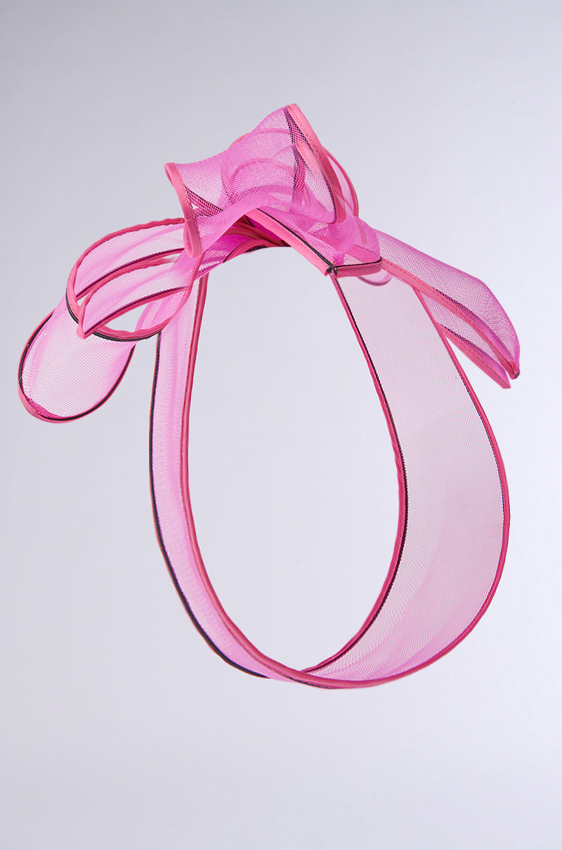 The TO THE RACES FASCINATOR IN PINK showcases a ribbon bow with translucent loops on a plain gray background, delivering a soft and elegant look. 3