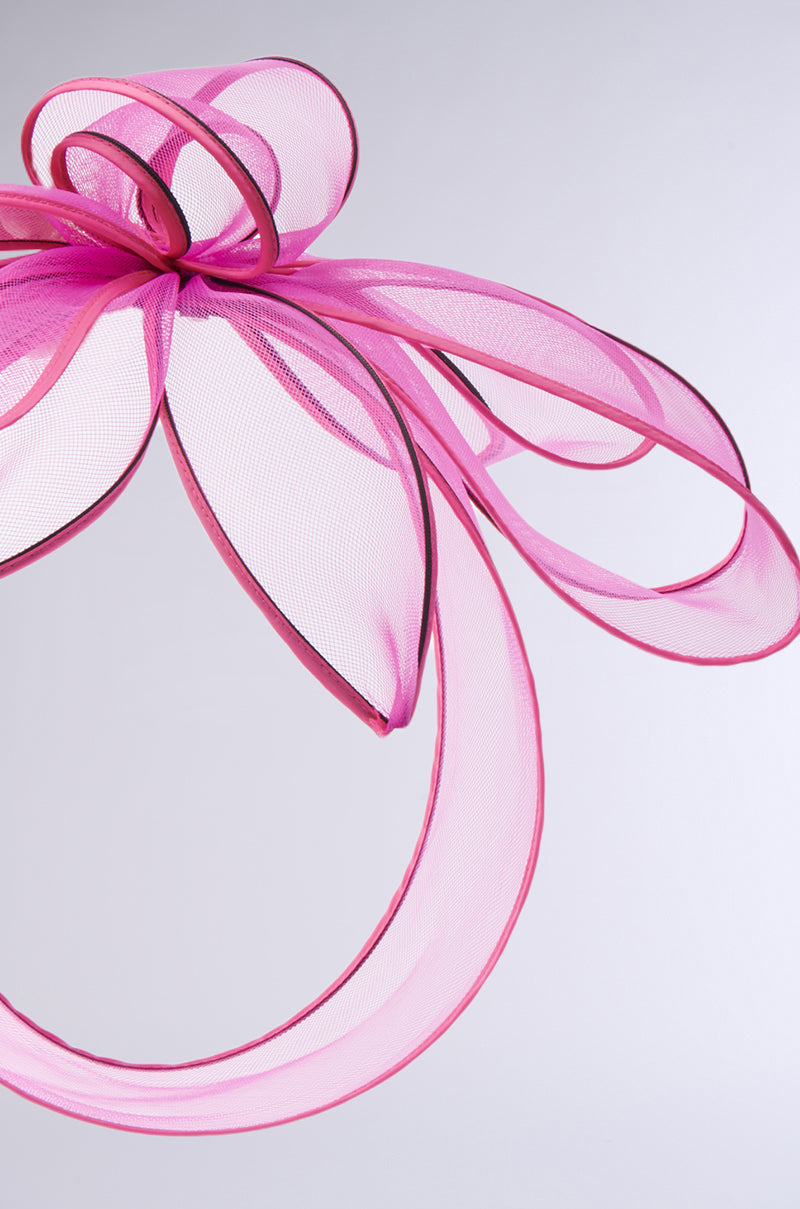 The TO THE RACES FASCINATOR IN PINK features an oversized, abstract pink bow of sheer material with dark edges, expertly crafted into loops and curves against a plain light gray background. 4
