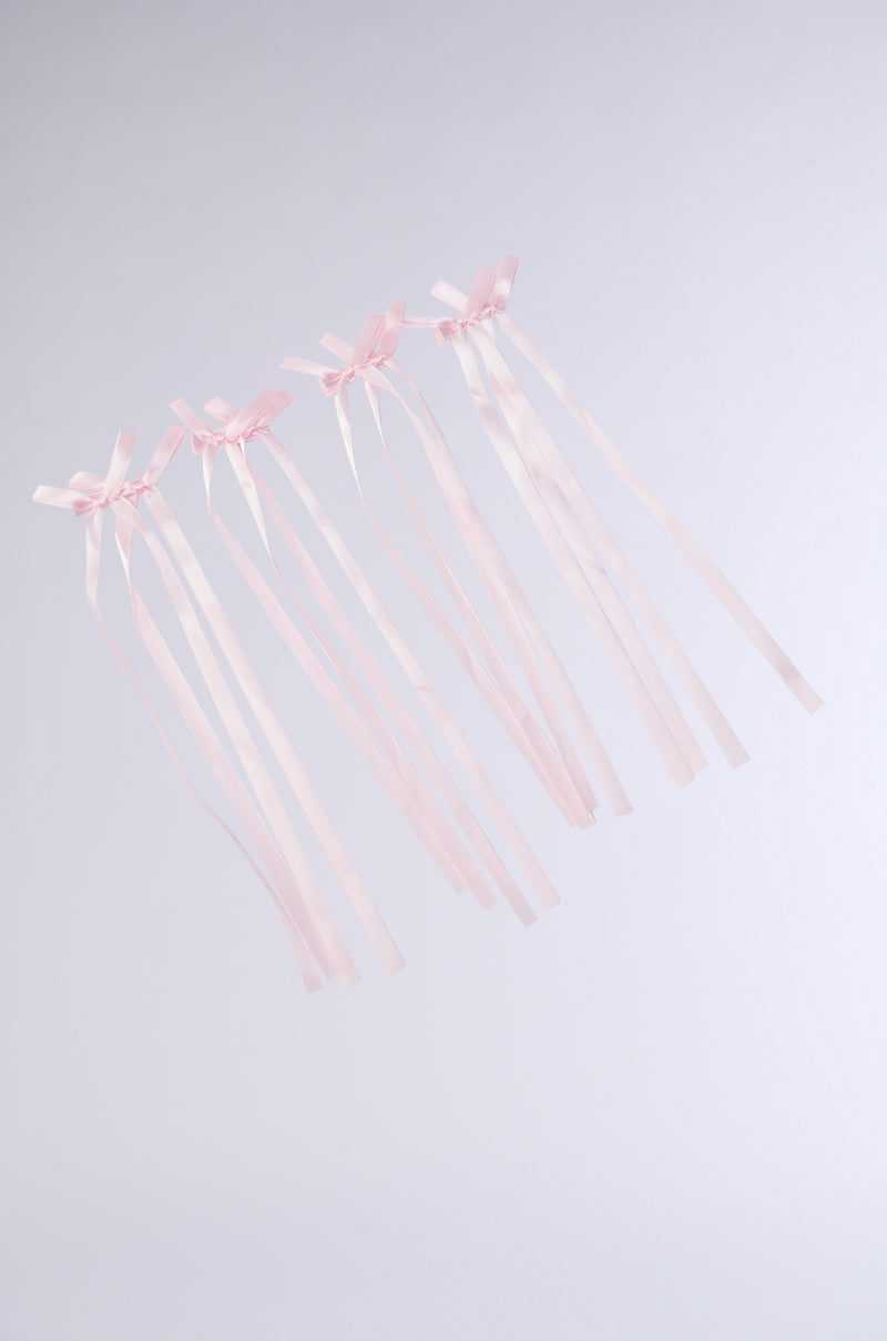 The CUTESY HAIR CLIP SET features five pink satin ribbon clips with bows extending vertically against a light gray background. The delicate hair clips exhibit thin strands flowing gracefully down, forming an elegant arrangement.