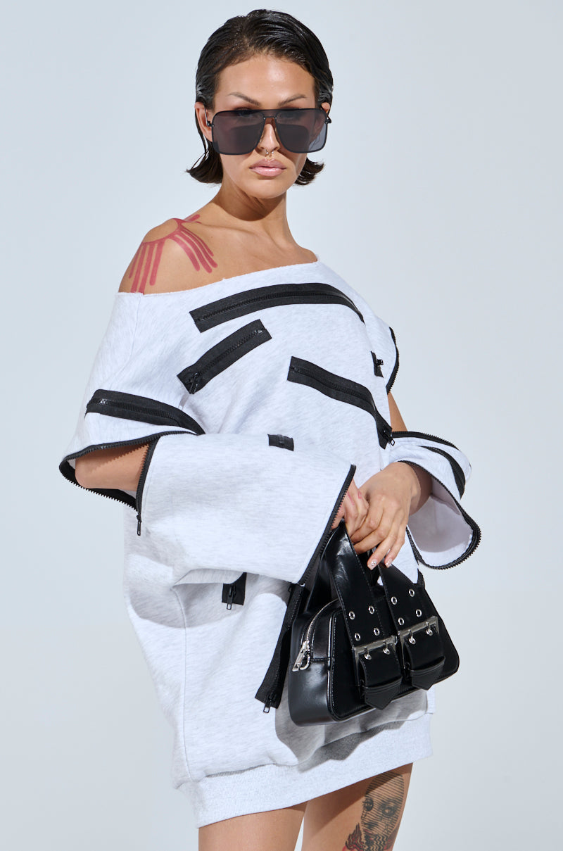 Sporting the ZIP ZAP OFF THE SHOULDER SWEATSHIRT DRESS-GREY MULTI, accessorized with large sunglasses and a black handbag, this style is enhanced by tattoos on legs and shoulders. The background remains plain.