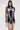 A woman poses against a plain background wearing the ALL ABOUT IT LACE UP MINI DRESS IN DENIM, a sleeveless dark denim mini dress with white lace-up details on the front. She carries a small silver handbag and has straight, center-parted dark hair.