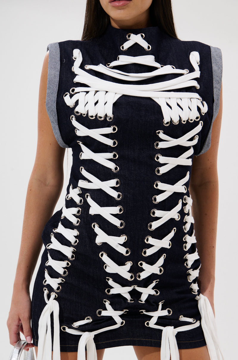 A woman wears the ALL ABOUT IT LACE UP MINI DRESS IN DENIM, a sleeveless dark denim mini with bold white lace-up detailing and metal eyelets across the front and sides for a modern corset-inspired look. 7