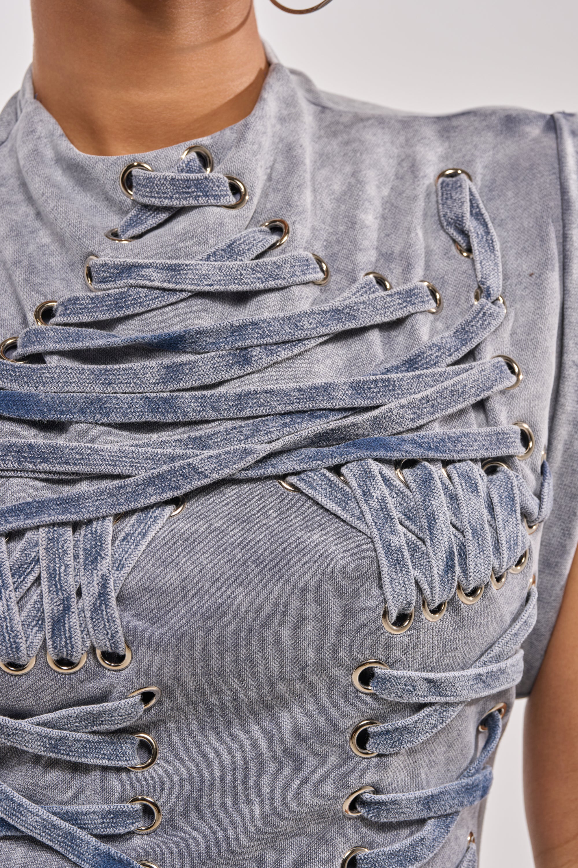 Close-up of the ALL ABOUT IT LACE UP MINI DRESS IN MEDIUM BLUE DENIM, featuring multiple crisscross laces threaded through metal eyelets for an intricate, textured look across the chest and shoulders. 5