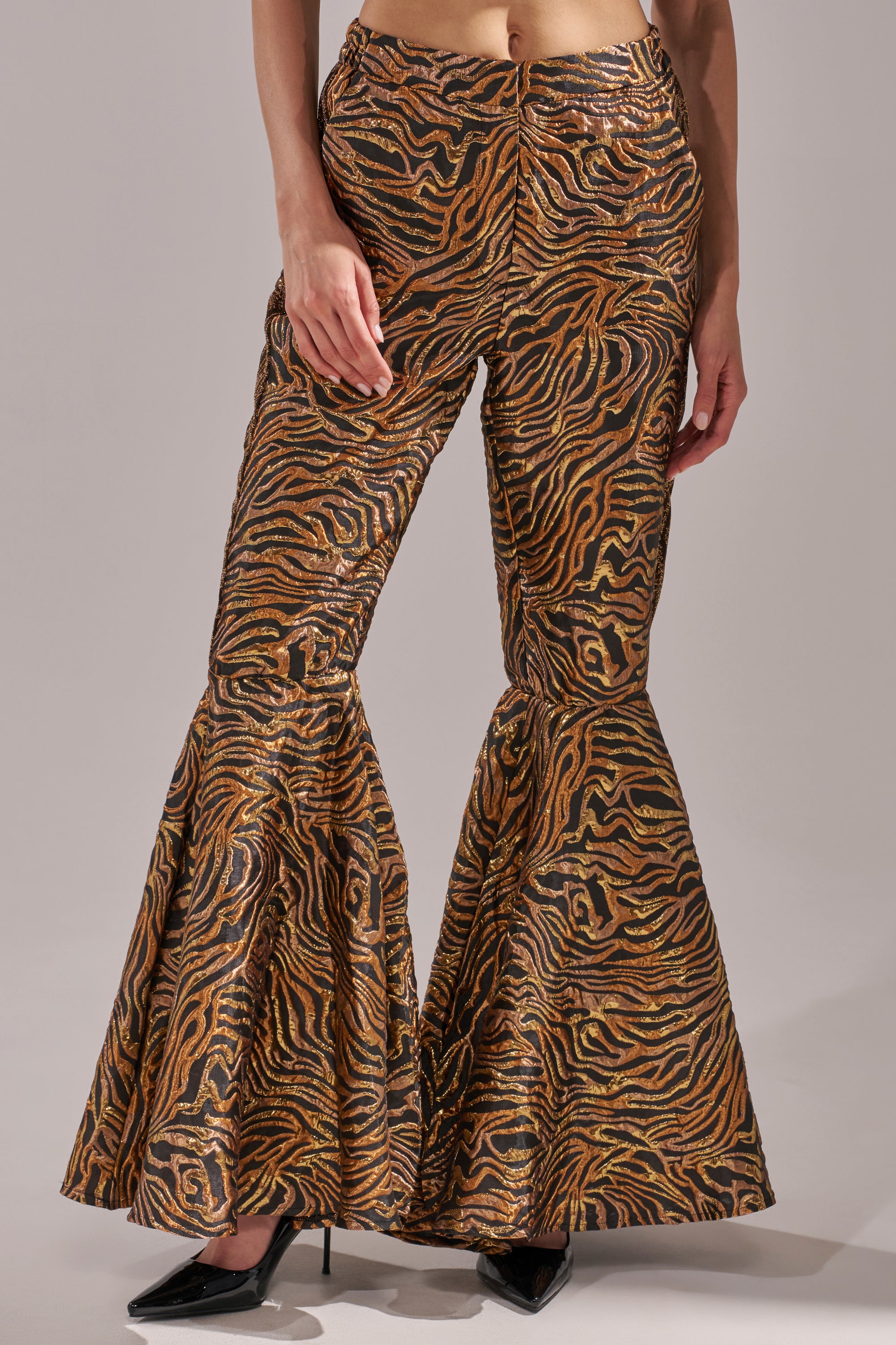 Wearing the GET IN MOTION BROCADE FLARE TROUSER with metallic tiger stripe jacquard and exaggerated flared legs, styled with black pointed heels; shown mid-torso down against a plain background. 3