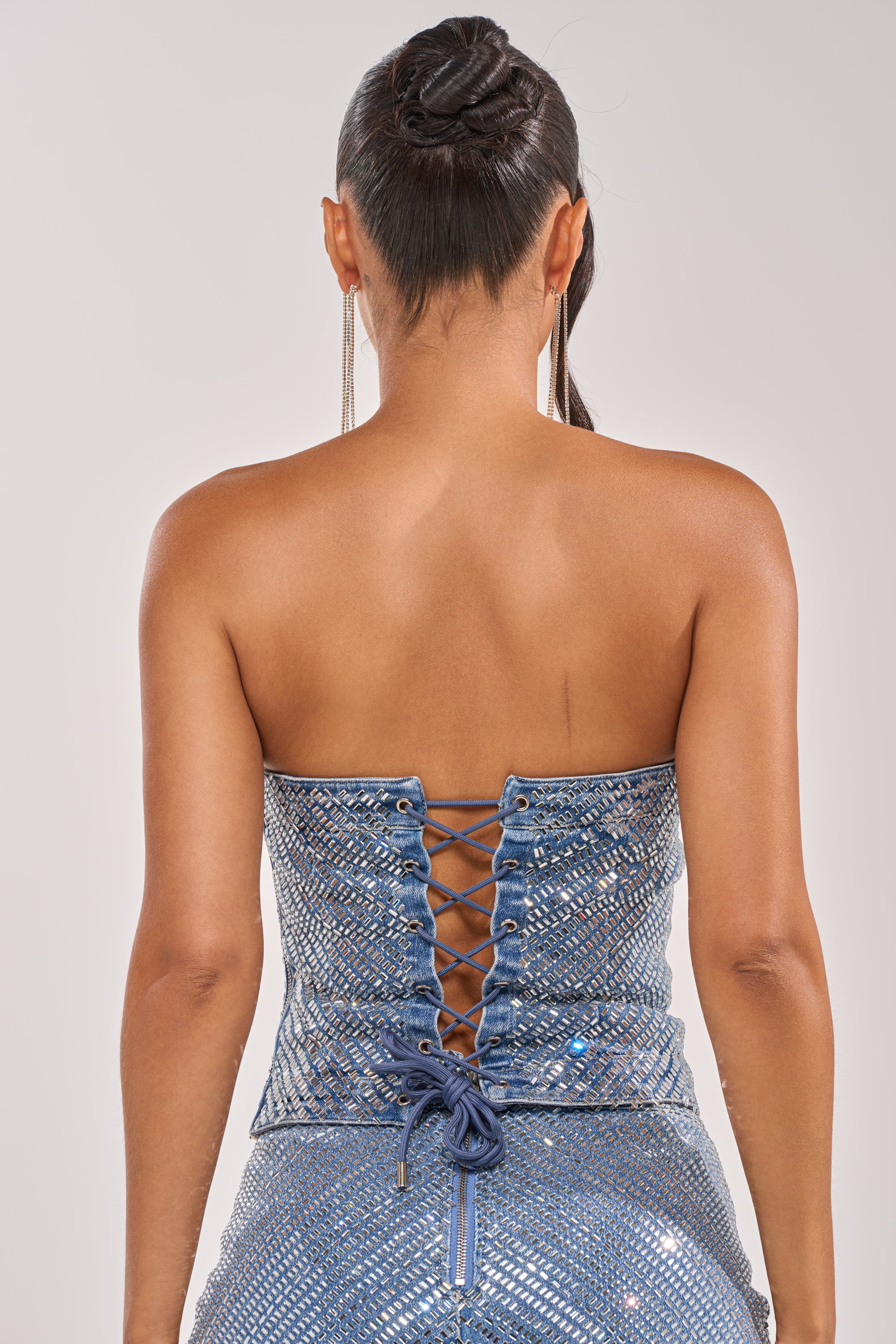 A woman seen from behind wears the BLING BLING CORSET, a sparkly blue dress with a sweetheart neckline, lace-up corset-style back, and her hair in an elegant updo. 7