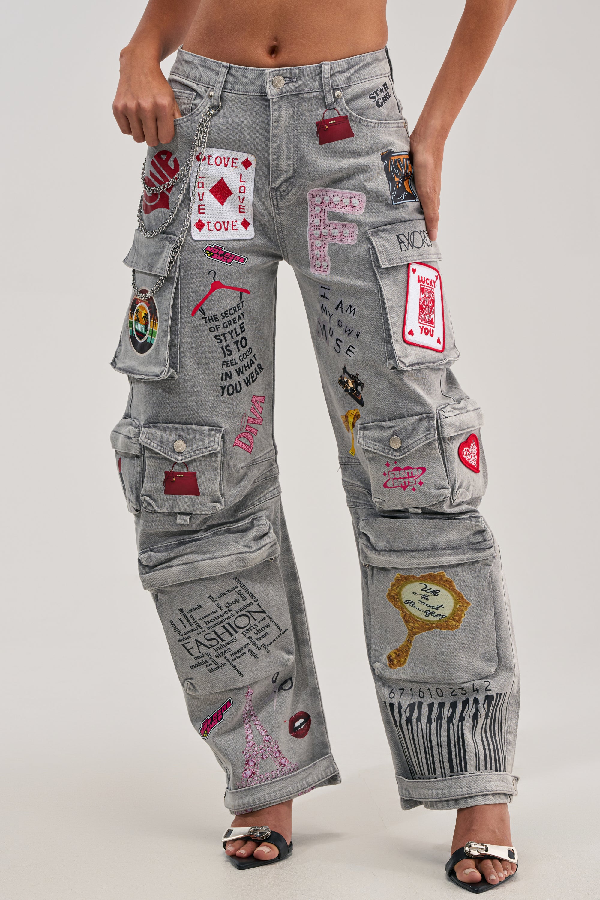 Someone wears the RAJ CARGO DENIM, grey denim cargo pants with colorful patches, doodles, playing cards, hearts, and artistic designs, styled boldly with black open-toe heels.